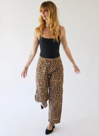 A woman modeling leopard-print wide-leg pants with a black camisole top and black pointed shoes, standing against a plain white studio background.
