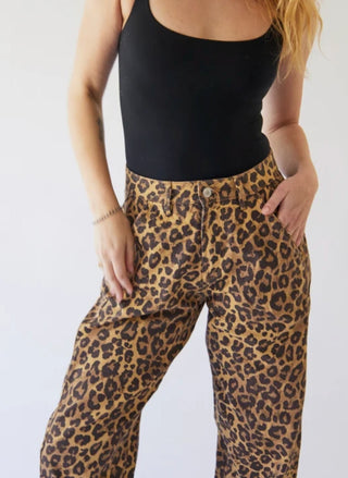 A person wearing leopard-print pants and a black tank top, cropped from the shoulders down against a plain light background.