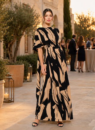 Woman wearing a black and camel abstract print sleeveless jumpsuit with a draped scarf-neck detail and wide-leg silhouette.