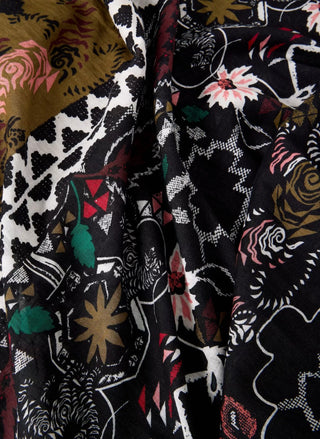 A close-up of a draped fabric with a complex, multicolor patchwork print featuring black, white, pink, green, and gold patterns.