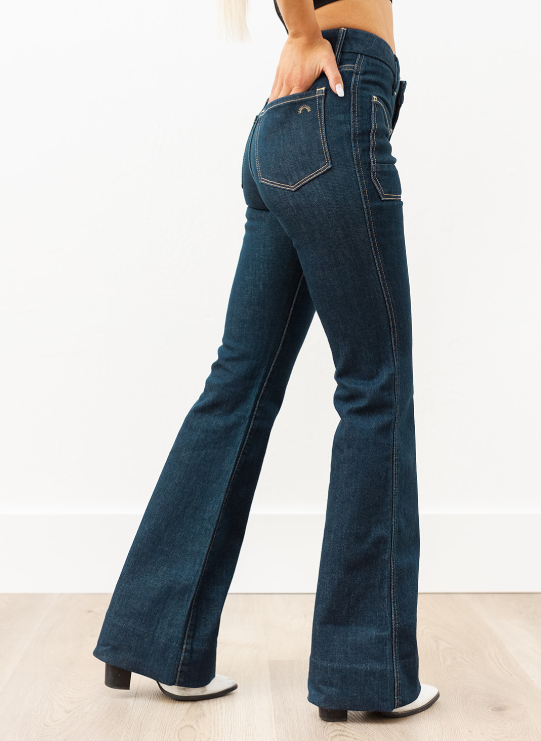 Side view of dark indigo Wanderer Flare jeans showing fitted thigh and true flared leg, styled with heeled boots.