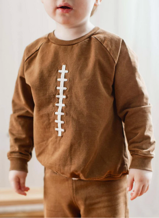 Child wearing a brown sweatshirt with a football design on a plain background