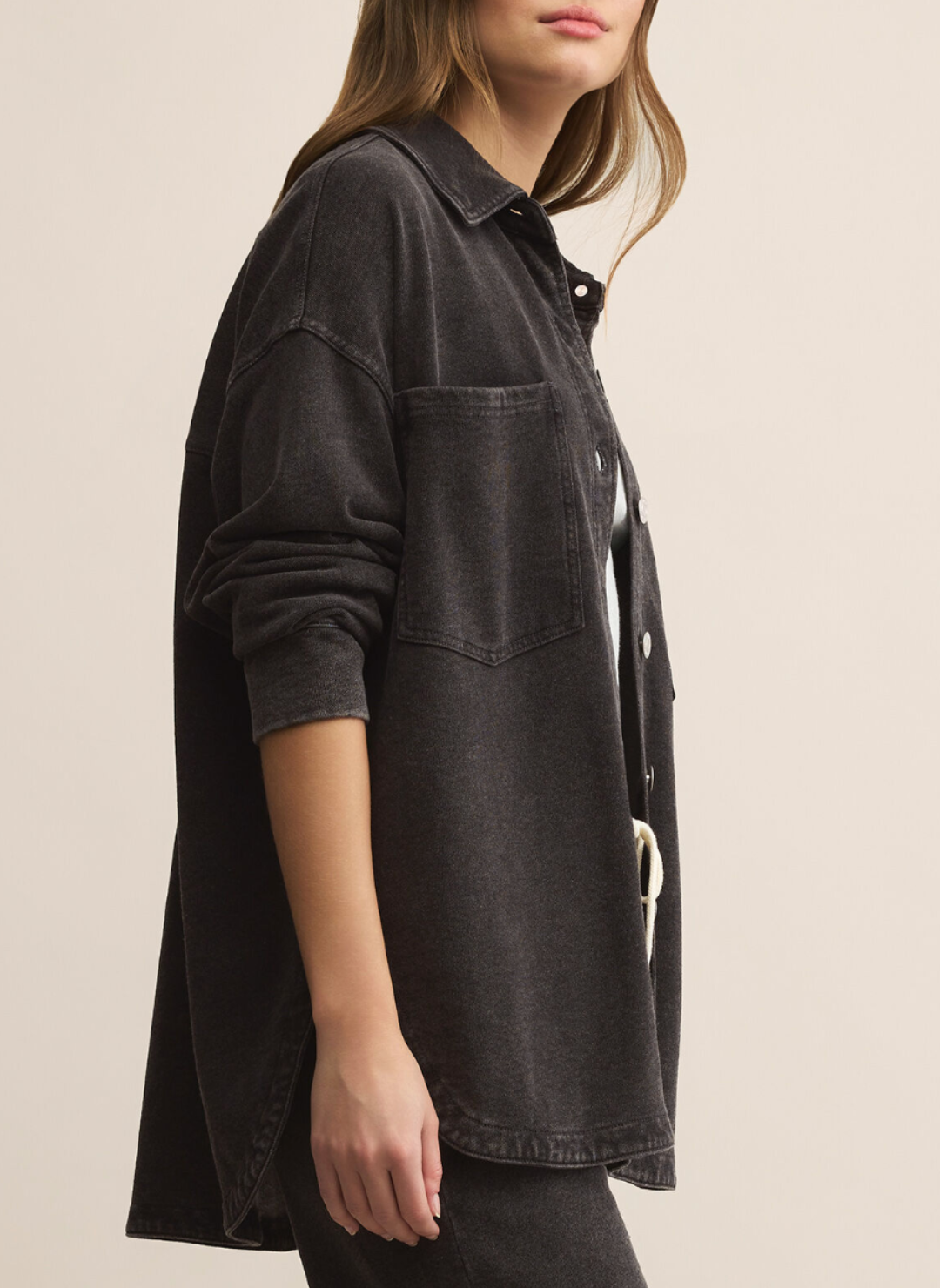 Person wearing a dark denim shirt with a belt on a beige background