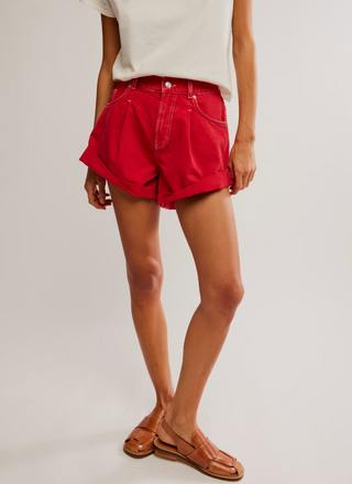 Front view of bright red high-rise denim shorts with raw hem, five-pocket styling, zip fly, and snug pull-on fit on a model’s hips.