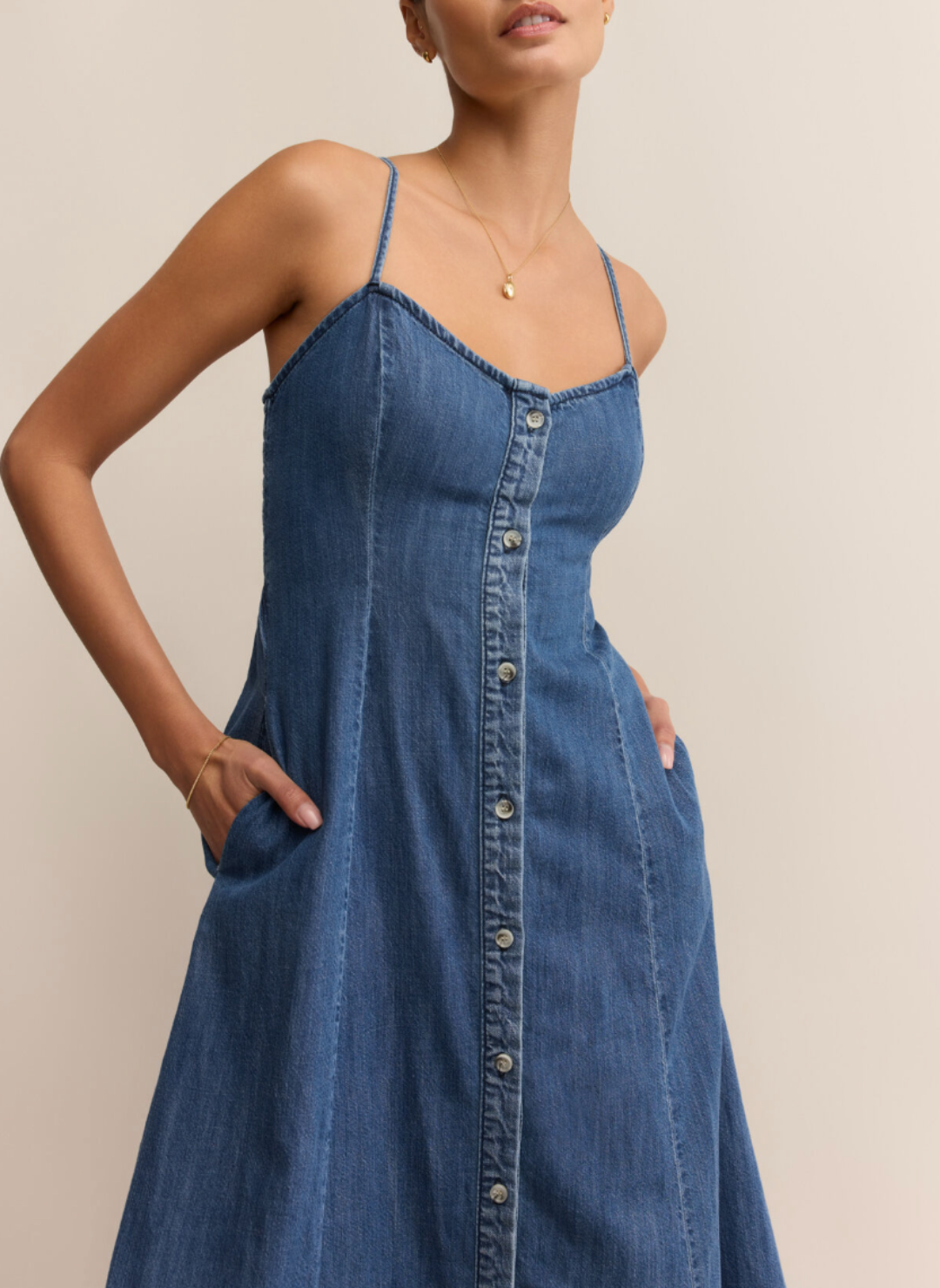 Woman wearing Z Supply Angel Eyes Denim Midi Dress with a sweetheart neckline, adjustable straps, front button detail, and flared hem; styled with tan boots.