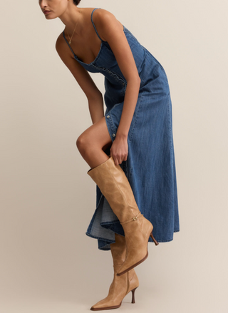 Woman wearing Z Supply Angel Eyes Denim Midi Dress with a sweetheart neckline, adjustable straps, front button detail, and flared hem; styled with tan boots.