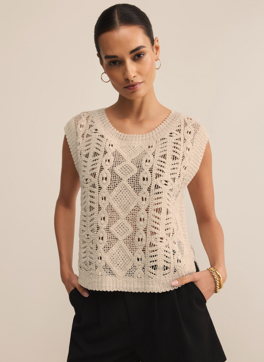 Alt Text: Woman wearing Z Supply Baroque Sweater Top in natural open-knit cotton with baroque-inspired pattern, styled with black shorts by the water.