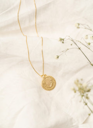 Gold necklace with a circular pendant on a light background