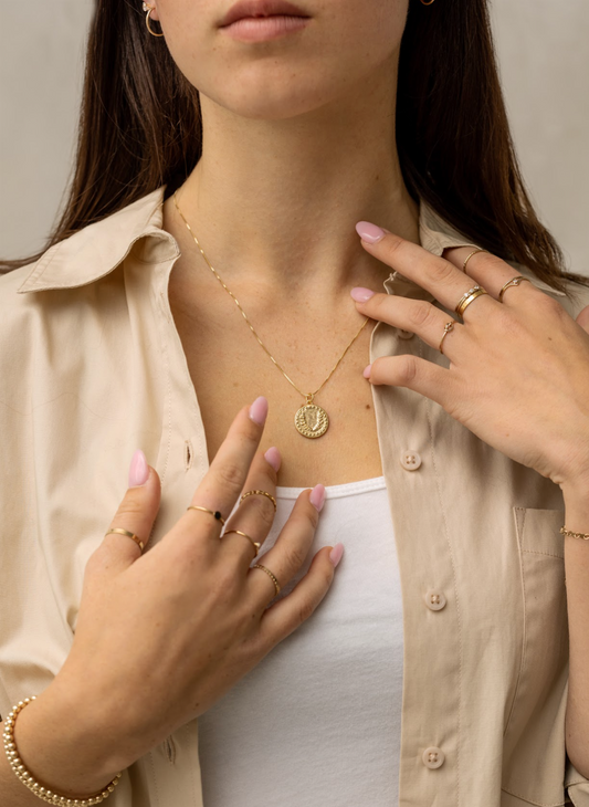 Woman wearing a gold necklace and multiple rings on a neutral background