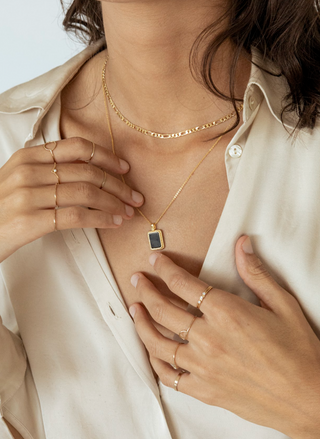 Person wearing a gold necklace with a square pendant, adjusting it with their hands.