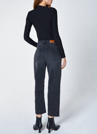 Person wearing a black long-sleeve top and dark gray jeans on a white background