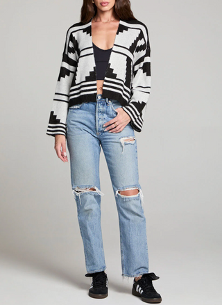 Person wearing a black and white patterned cardigan with ripped jeans on a gray background