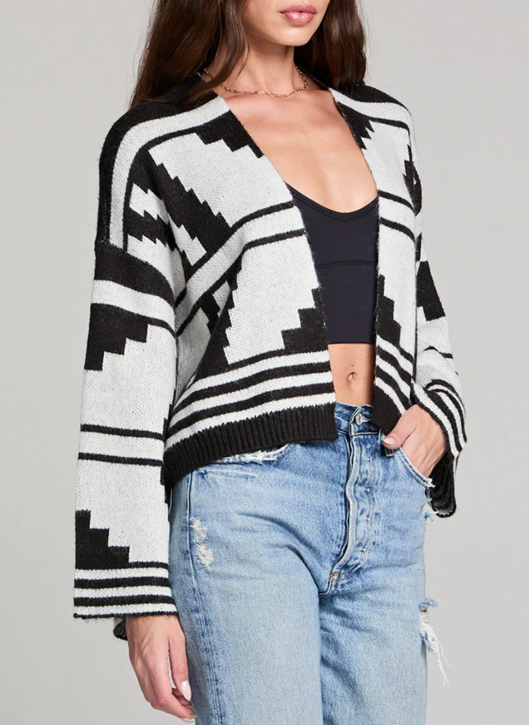 Woman wearing black and ivory Saltwater Luxe Southwest Cardi with geometric print, cropped length, and flared sleeves paired with high-waisted jeans.
