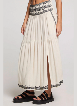 Long white dress with black embroidery and a slit, paired with black sandals on a light gray background.