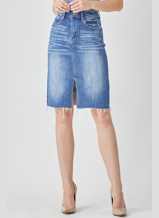 Blue denim skirt worn by a person on a white background.  Tabitha high rise denim pencil skirt with front slit and raw hem in medium wash, hits above the knee, stretch fit.