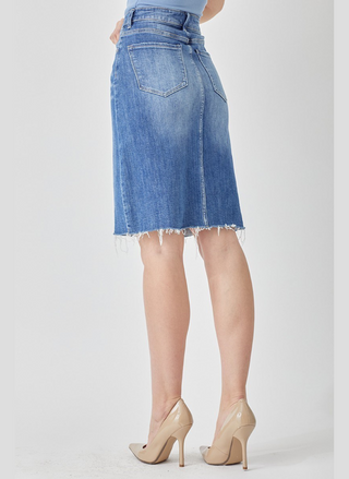 Blue denim skirt worn by a person on a white background.  Tabitha high rise denim pencil skirt with front slit and raw hem in medium wash, hits above the knee, stretch fit.