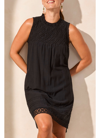 Woman wearing a black sleeveless dress with lace trim against a neutral background