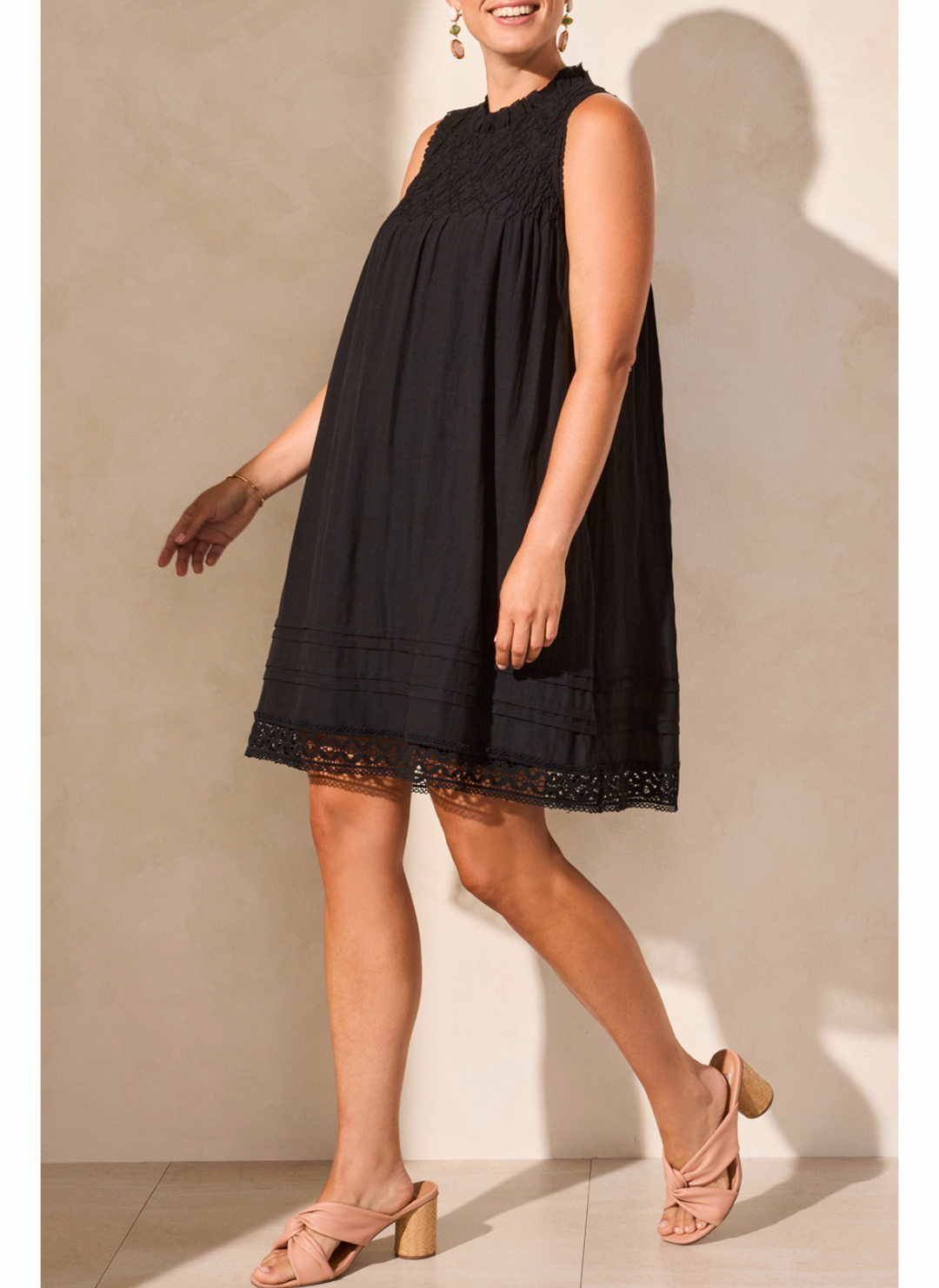 Woman wearing a black dress with lace details against a beige wall.