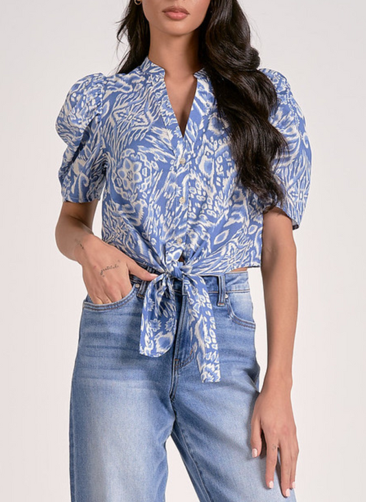Blue and white ikat print short-sleeve blouse with puff shoulders, button-front closure, and front tie hem, shown with light wash denim jeans for a breezy, coastal-inspired look.