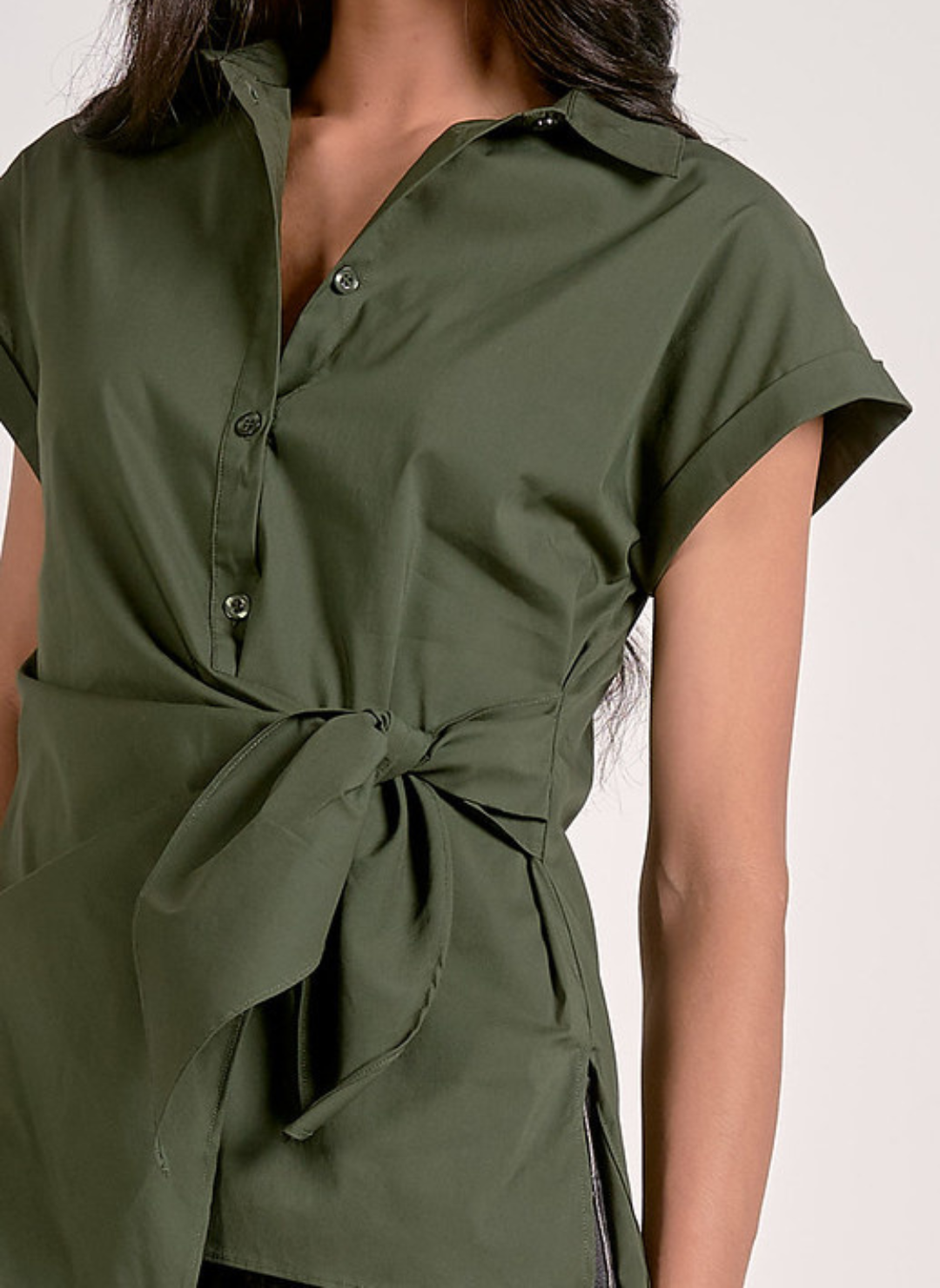 Close up view of olive green short-sleeve button-up blouse with a collared neckline, front tie waist detail, and tailored fit, styled with dark wash jeans for a chic casual look.
