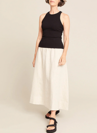 Woman wearing a black sleeveless top and white skirt on a beige background