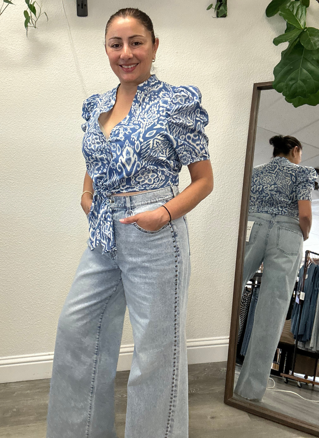 Woman wearing a blue patterned top and light blue jeans with studs going down the side seams, standing in front of a mirror.