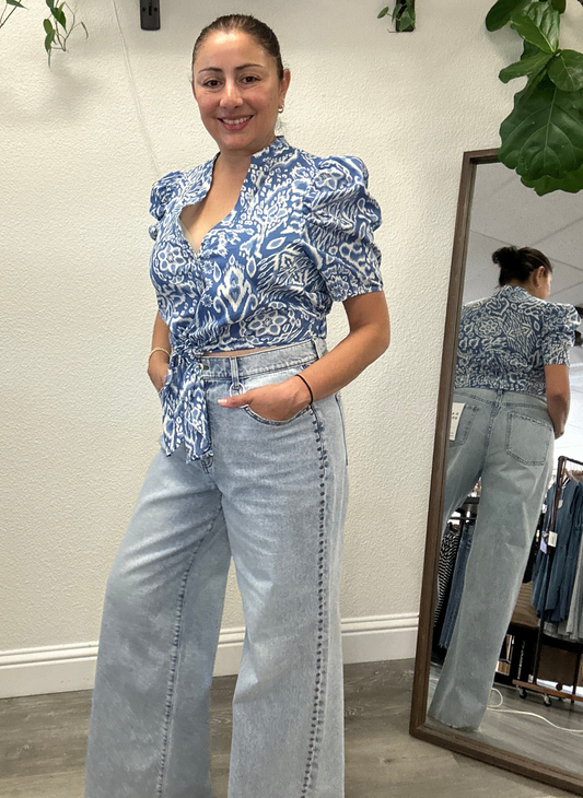 Woman wearing a blue patterned top and light blue jeans with studs going down the side seams, standing in front of a mirror.