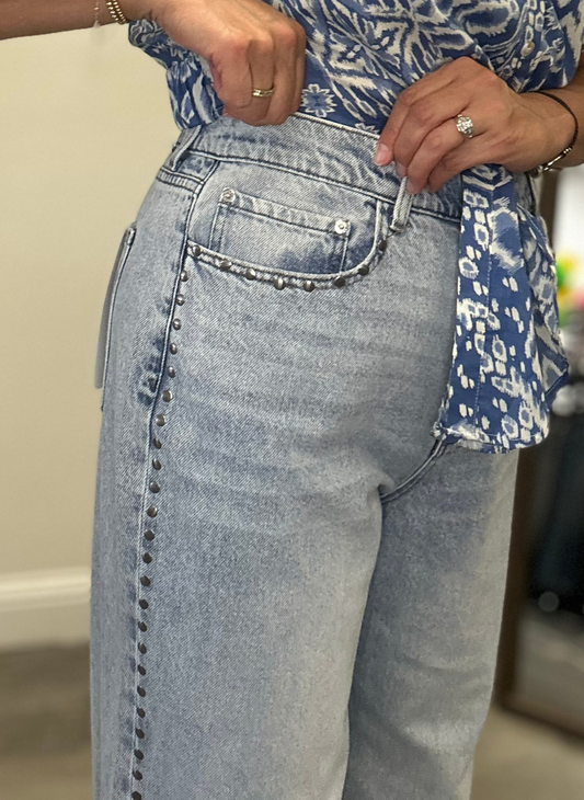 Close-up of light blue studded jeans with a patterned shirt.  The studs outline the pocket and continue down the side seam.