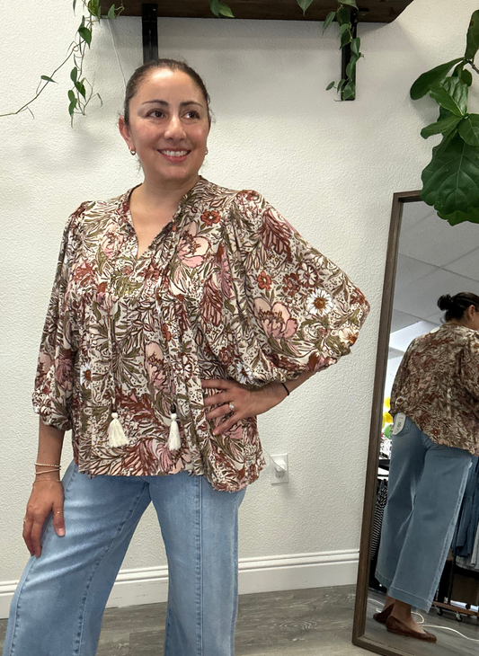 Bethany Bohemian Floral Peasant Blouse in lightweight rayon crinkle with tassel-tie split neckline and 3/4 balloon sleeves, styled with light denim jeans.  Woman wearing the floral blouse and blue jeans standing in front of a mirror.