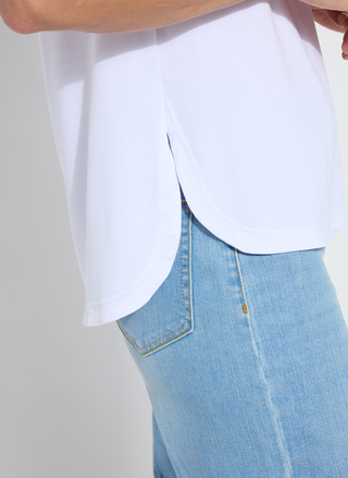 Woman wearing the Lyssé Katarina Eyelet Sleeve Trim Top in white; features embroidered floral eyelet cap sleeves, crew neckline, and a rounded shirttail hem. Lightweight and feminine, available at August Boutique Ripon.