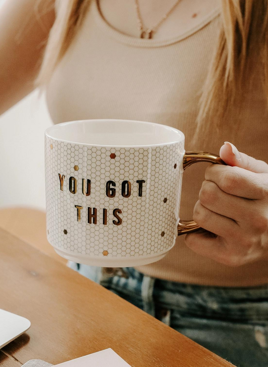 Up close view of You Got This mug. Model is wearing a beige tank top and denim jeans while holding the mug. 