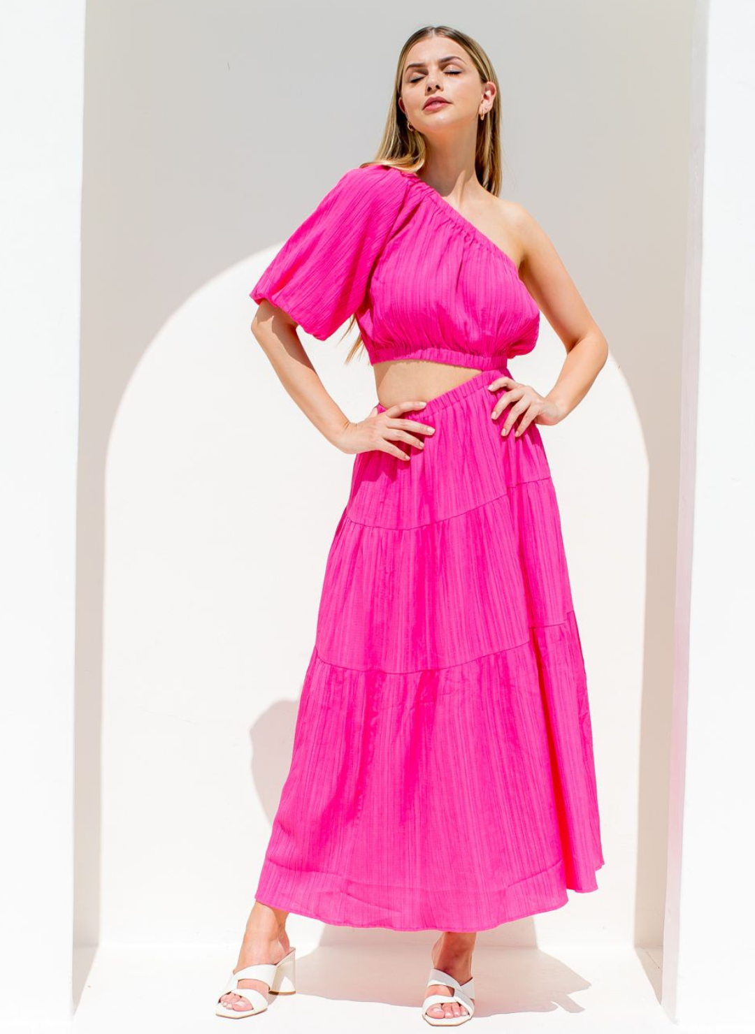 Model with hands on hips wearing fuchsia vibrant Grecian Dream Maxi Dress with one shoulder design and waist cutout detail.