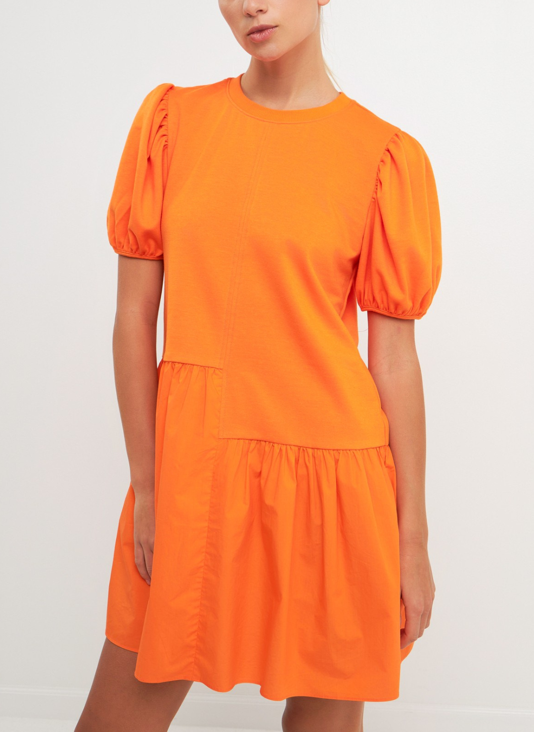 Model wearing Orangesicle Delight Dress with short puffy sleeves, knit bodice, cotton poplin skirt, and uneven front seam at the waist. White background.