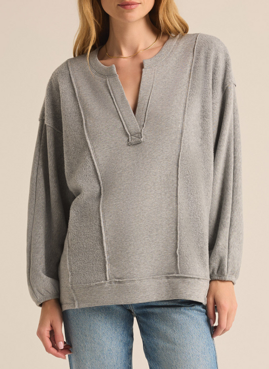 Model is wearing Out Of Towner Sweatshirt with denim jeans and arms by side showing the lined and textured detail in the material and V-neckline. Front view with white background.  