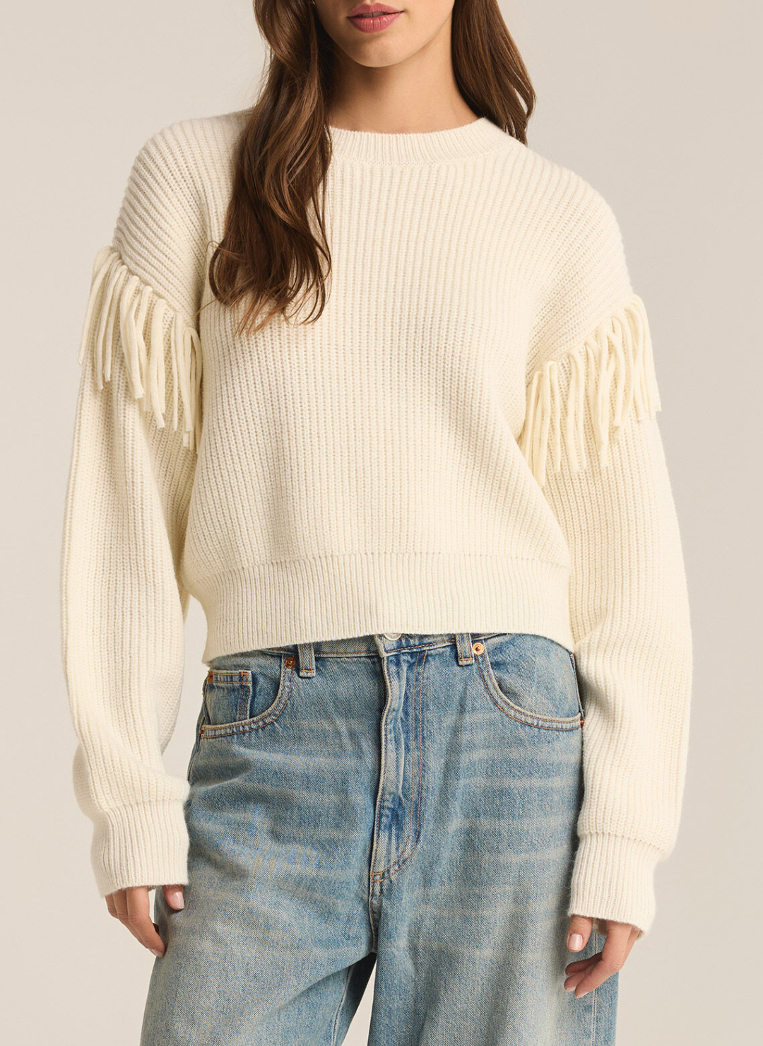 Model is wearing On the Fringe sweater paired with denim jeans displaying the detailed fringe on sleeves. Front view with white background.