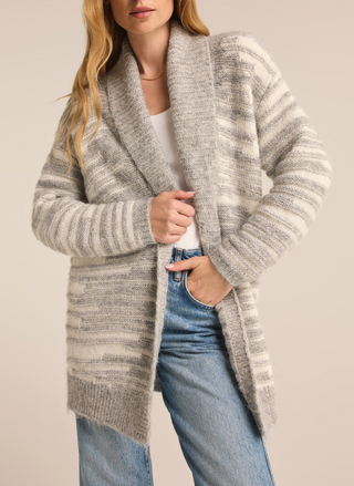 Model is wearing Level Up Cardigan with on hand in pocket of jeans and one arm holding cardigan. Model is wearing a white top underneath. Front view.