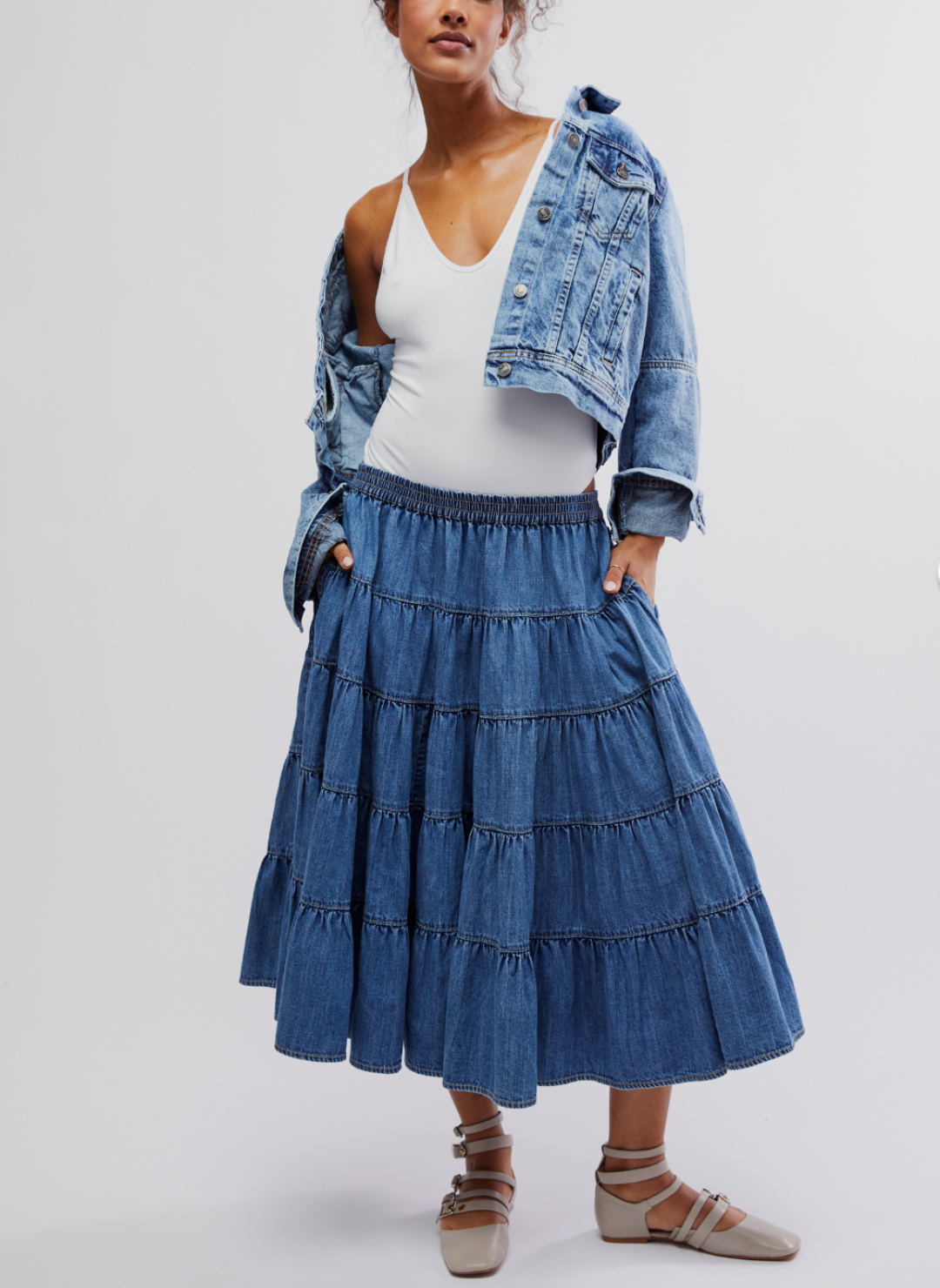 Full view of Swing Denim Skirt. Model is wearing a white body suit under a denim jacket. 