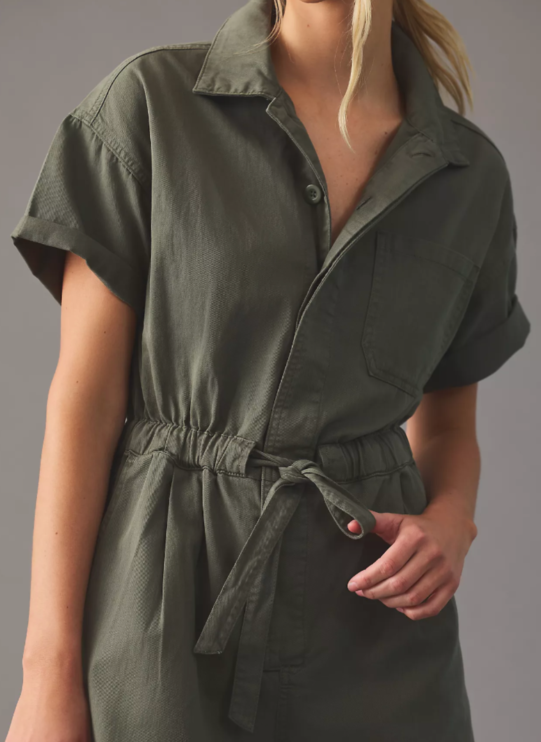 Close up view of army green romper with top button undone and a bow tied in the front of waistband.