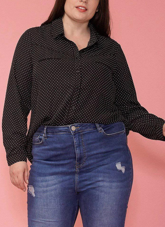 Front view of model wearing PLUS - Spot On Blouse that is a black button up with small white polka dots. Blouse is paired with darker washed jeans. One hand by side with a pink background. 