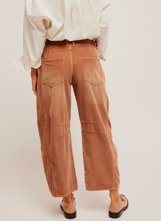 Back View: Pictured a corduroy pant in a rust color.  Darts at the inner knee and a tapered hem.  White shirt paired with it and loafers.