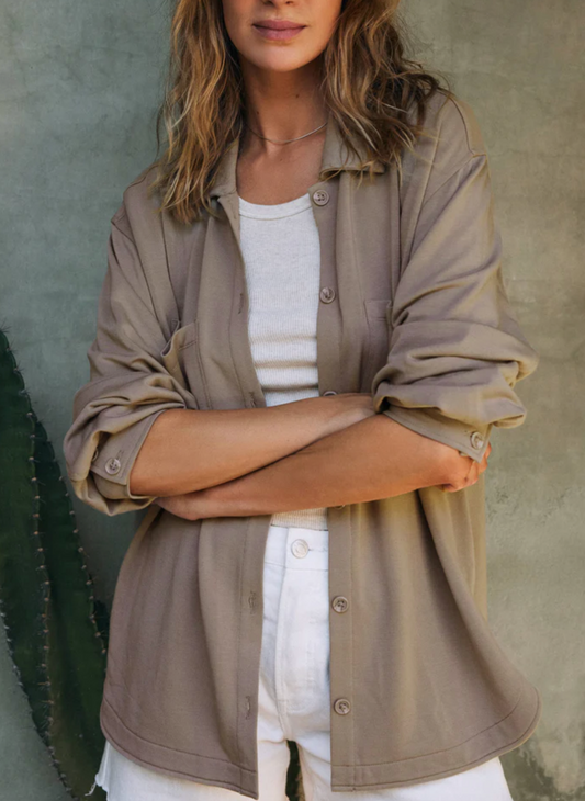 The model shows the front profile of the light brown button up with a white shirt underneath. With the sleeves pulled up to her elbows.