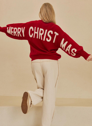 Image shows model with arms out, wearing a red sweater that says Merry Christmas across the back. Red Christmas Cool Sweater with MERRY CHRISTMAS graphic back view. 