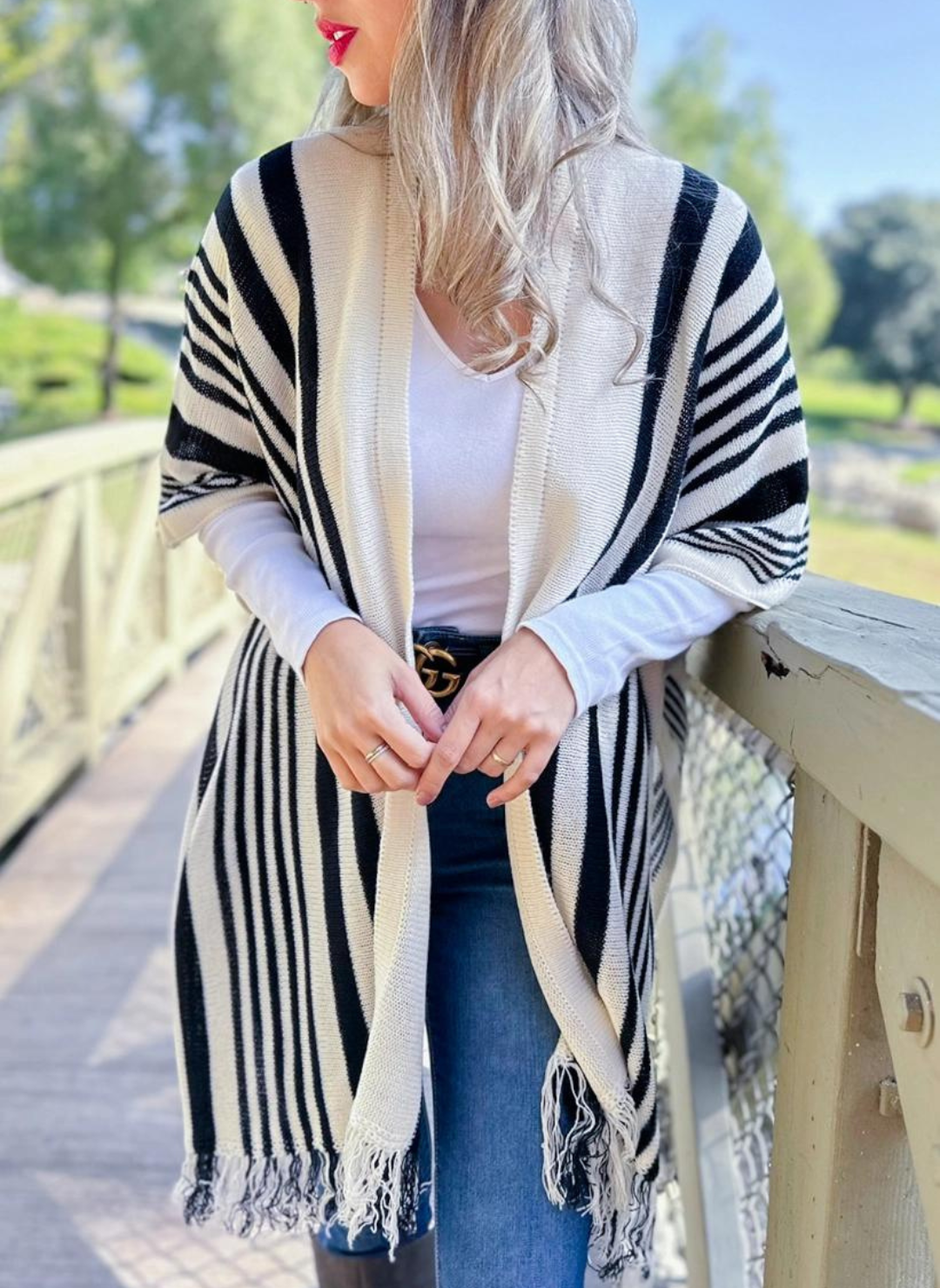 The model is wearing a stripe printed lightweight knit kimono cardigan with tassel with white shirt underneath with black belt and blue jeans.