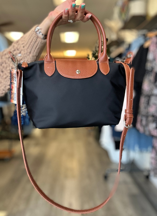 Image of black bag with brown leather handles, closure and long strap.