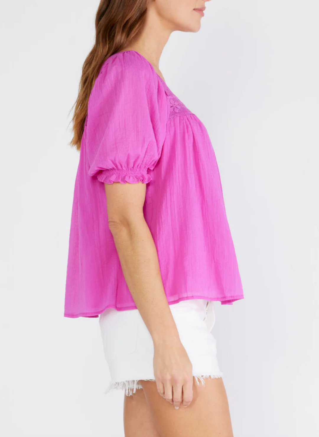 Side view of model wearing fuchsia LS  Perry Puff Sleeve Top with lace square neckline, slight puff in the half sleeve and a fully lined bodice styled with white shorts.