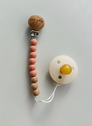 Pacifier clip with wooden beads and a white pacifier on a light gray background