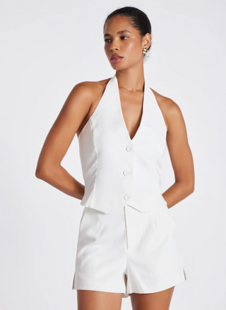 Model View: Woman wearing the Porto Vest by Bishop & Young in white—halter neckline, deep V-front with three buttons, paired with matching high-waist white shorts.