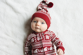 Baby wearing a red and white patterned sweater and hat on a white blanket