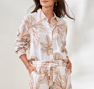 Woman wearing a white outfit with brown floral patterns on a plain background