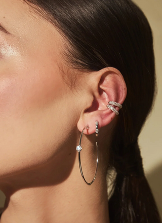 Side profile of a model with dark hair wearing the silver FYB Tory Ear Cuff with sparkling clear stones, paired with delicate silver earrings.